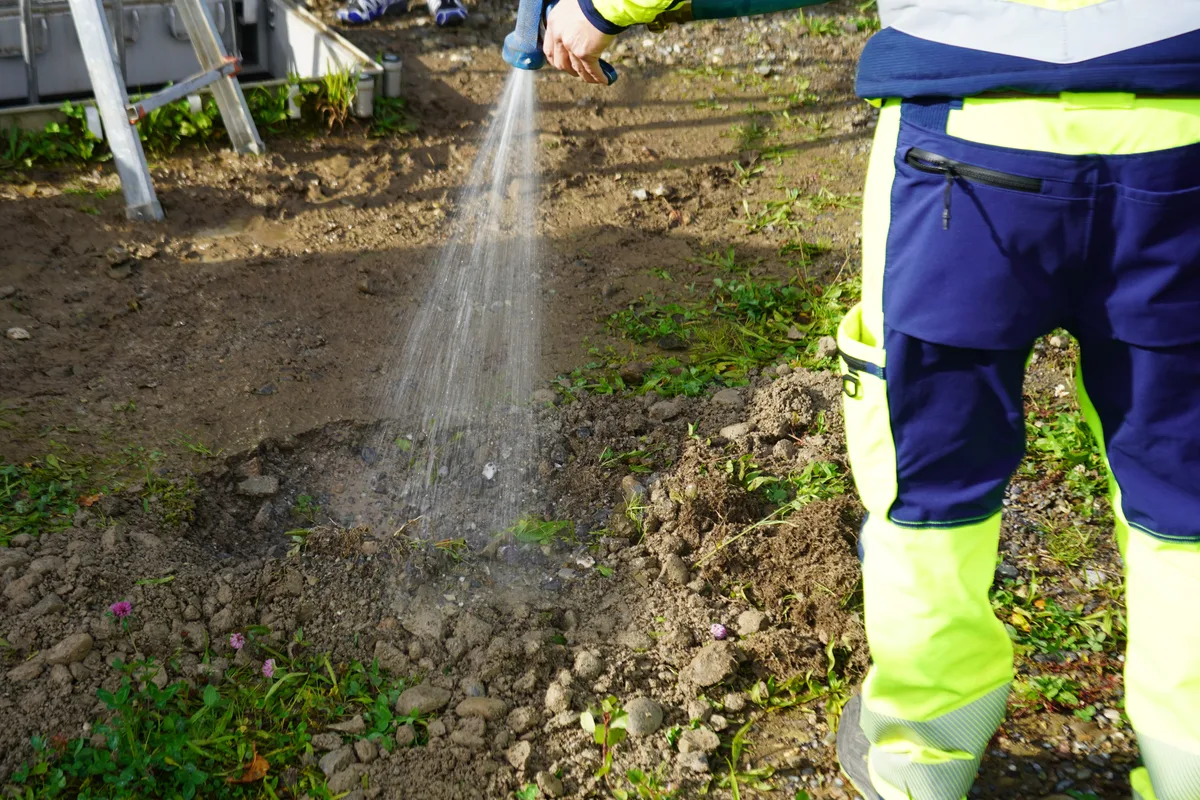 Man sieht eine Person, die eine Pfütze im Boden mit Wasser füllt.